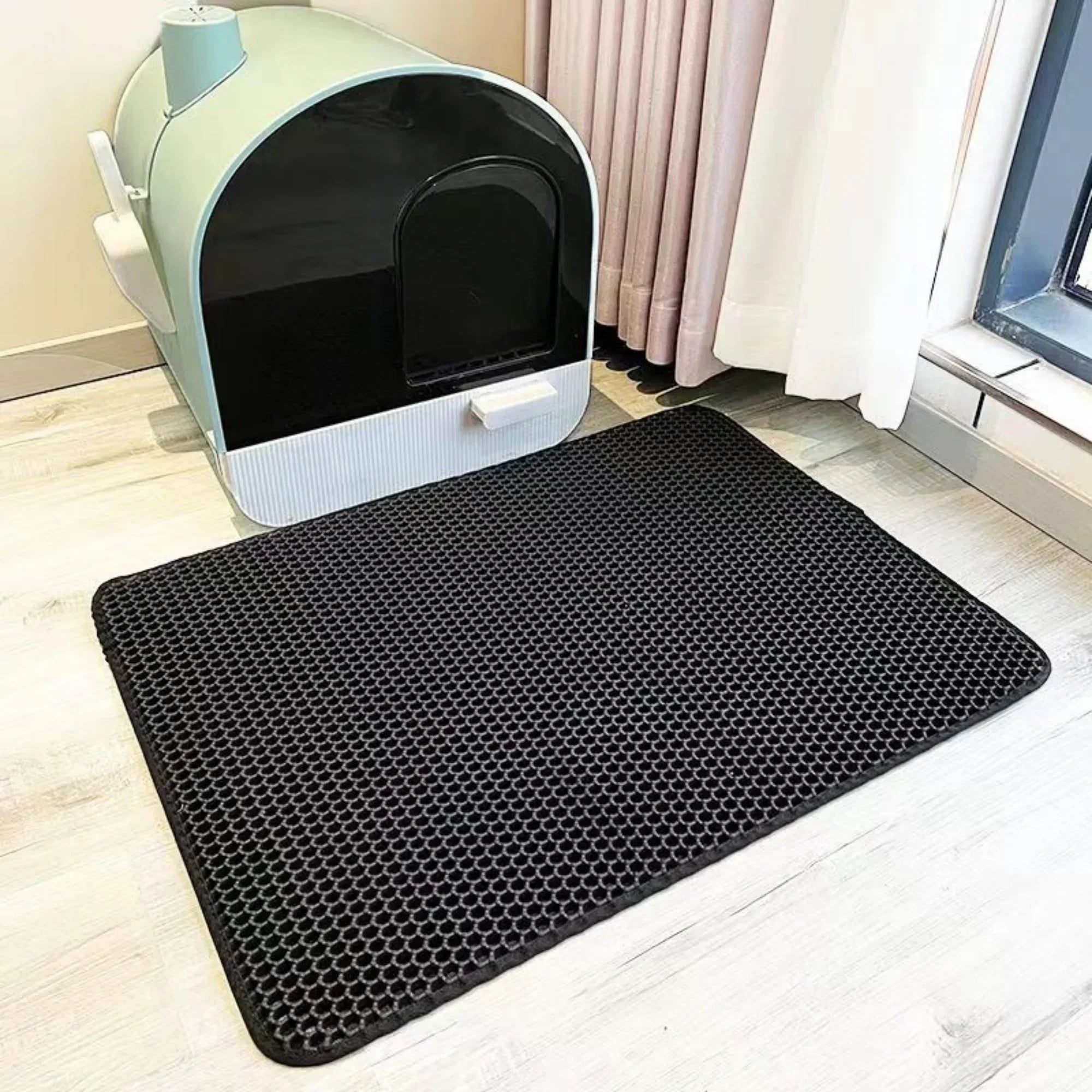 Black honeycomb mat in front of a cat litter box on a light wood floor.