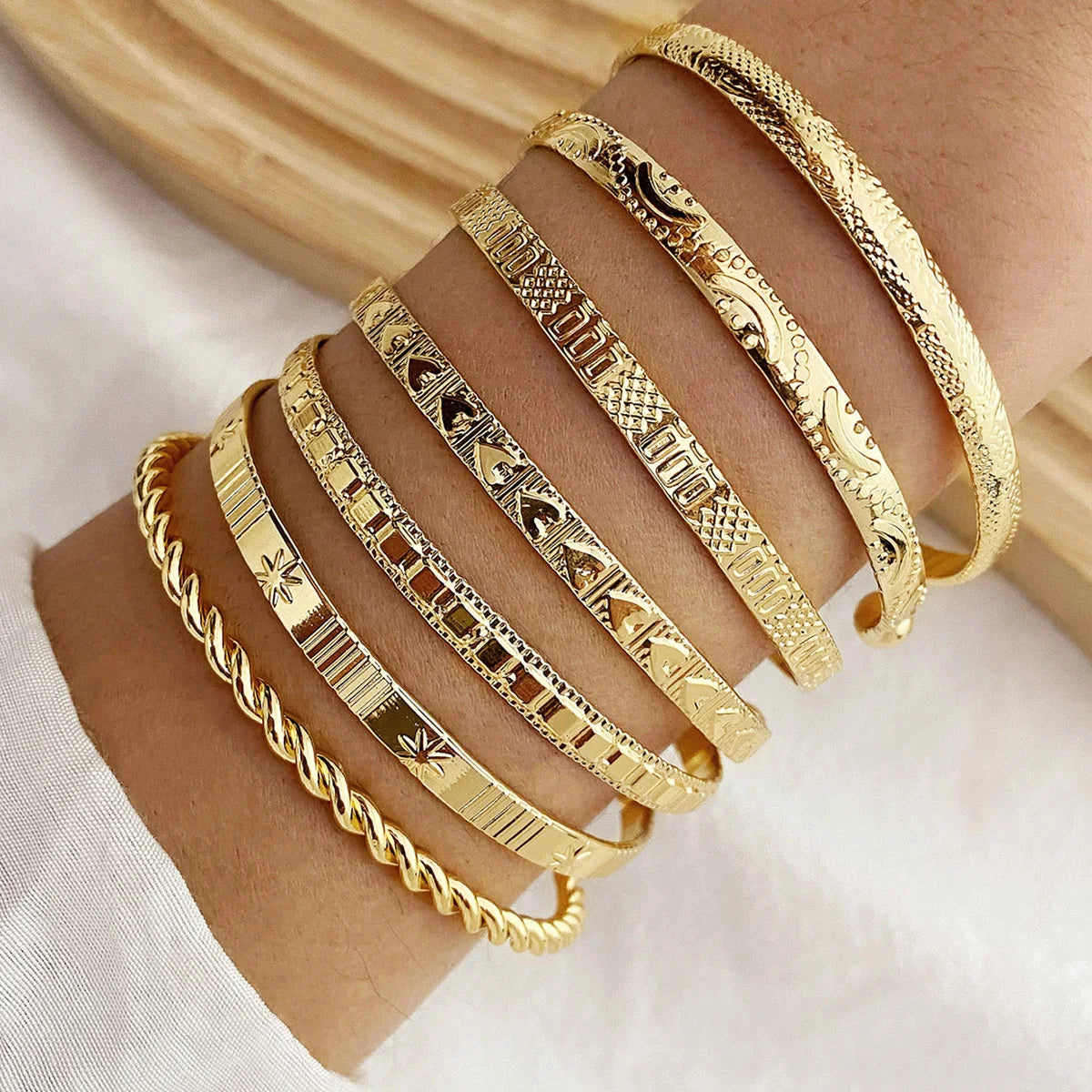 Gold bracelets with various patterns on a wrist against a light background