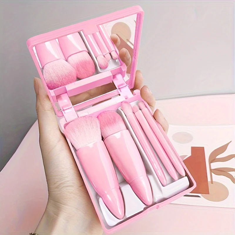 Pink makeup set with brushes and mirror held in a hand against a neutral background