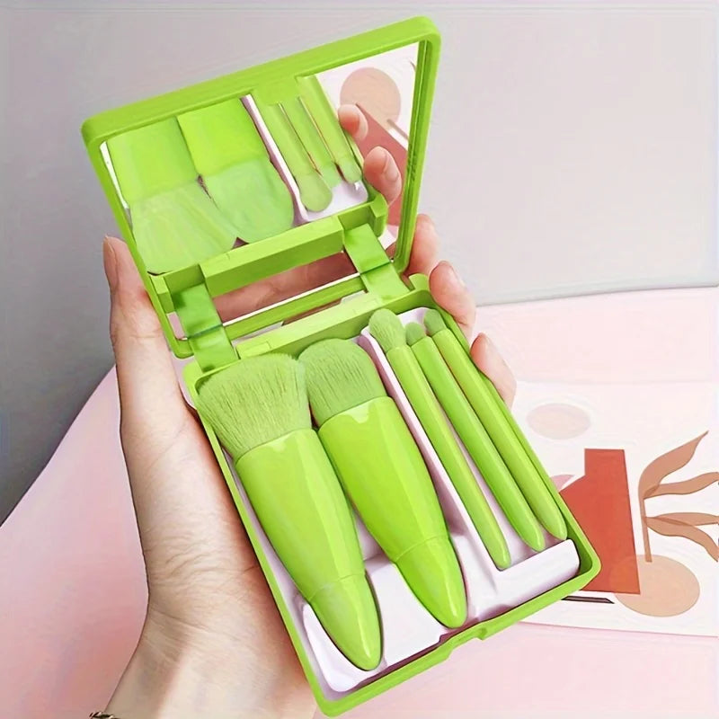 Set of green makeup brushes in a compact case held by a hand against a light background