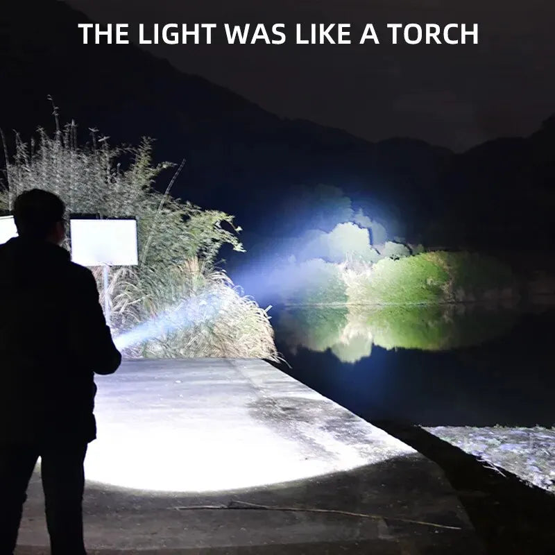 Person holding a flashlight on a wooden path with a reflective surface and mountains in the background.