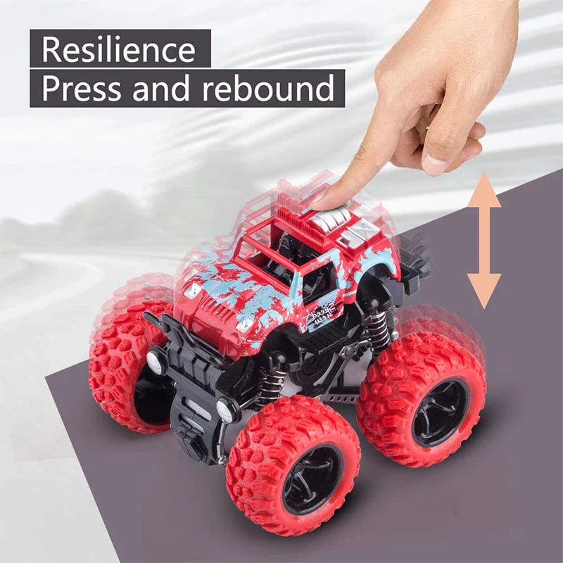 Red toy monster truck with large wheels on a gray surface, being pressed by a hand.