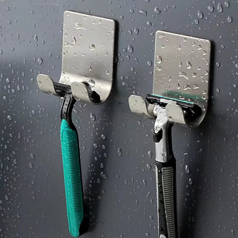 Two razors attached to metal hooks on a wet bathroom wall.