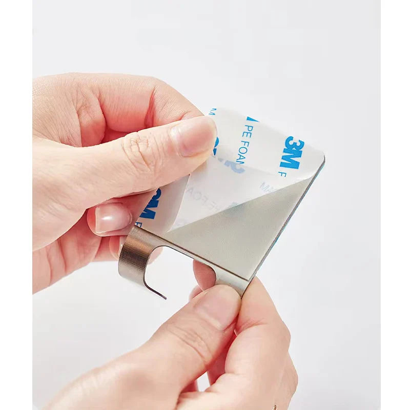 Person using a metal tool to peel off a strip of tape with '3M' branding on a white background.