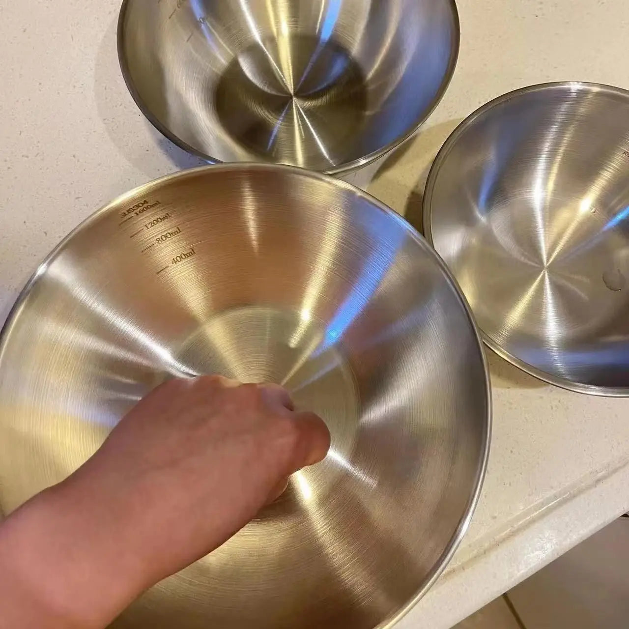 Three metal bowls on a light-colored surface with a hand touching one of them.
